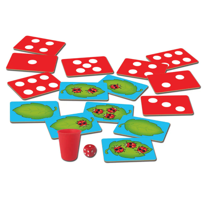 Board game components including red dice, green leaf cards with ladybugs, and a red cup on a white background.