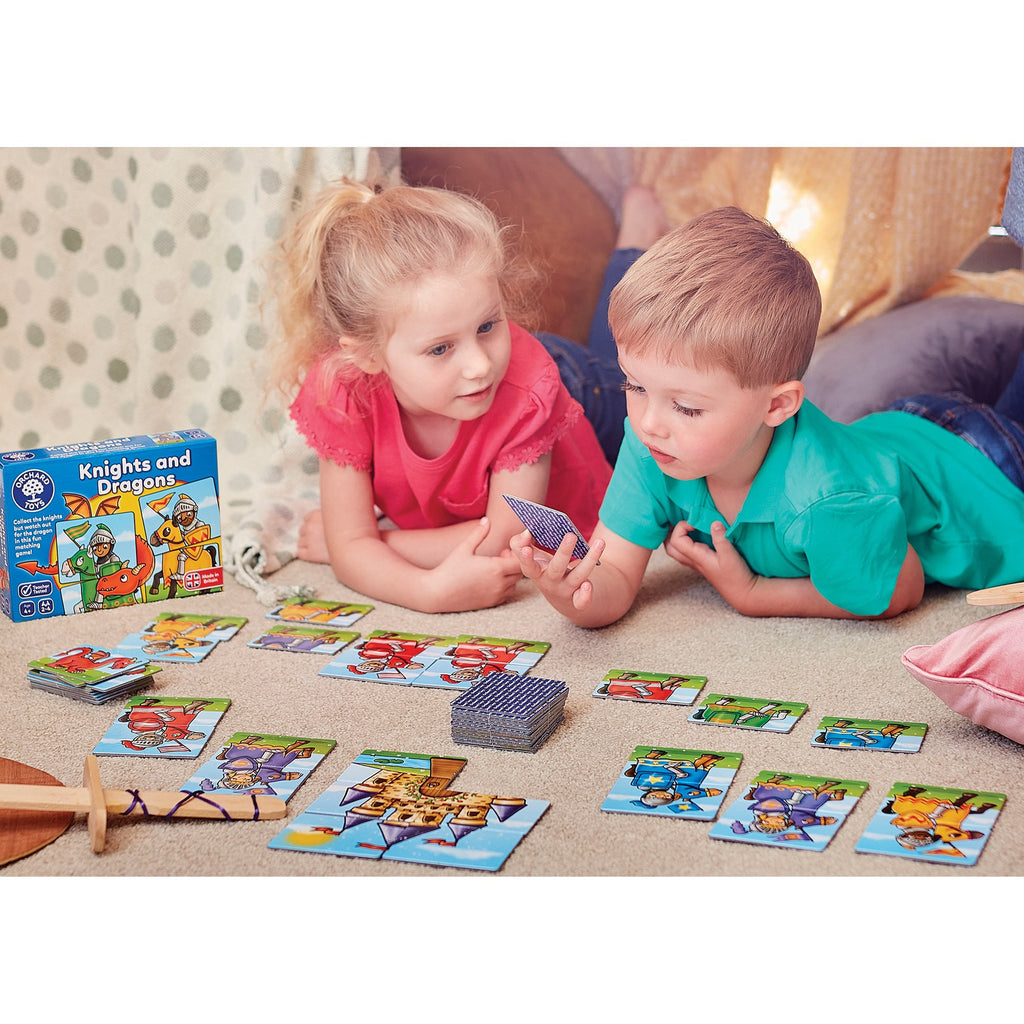 Two children playing with a 'Knights and Dragons' card game on the floor.