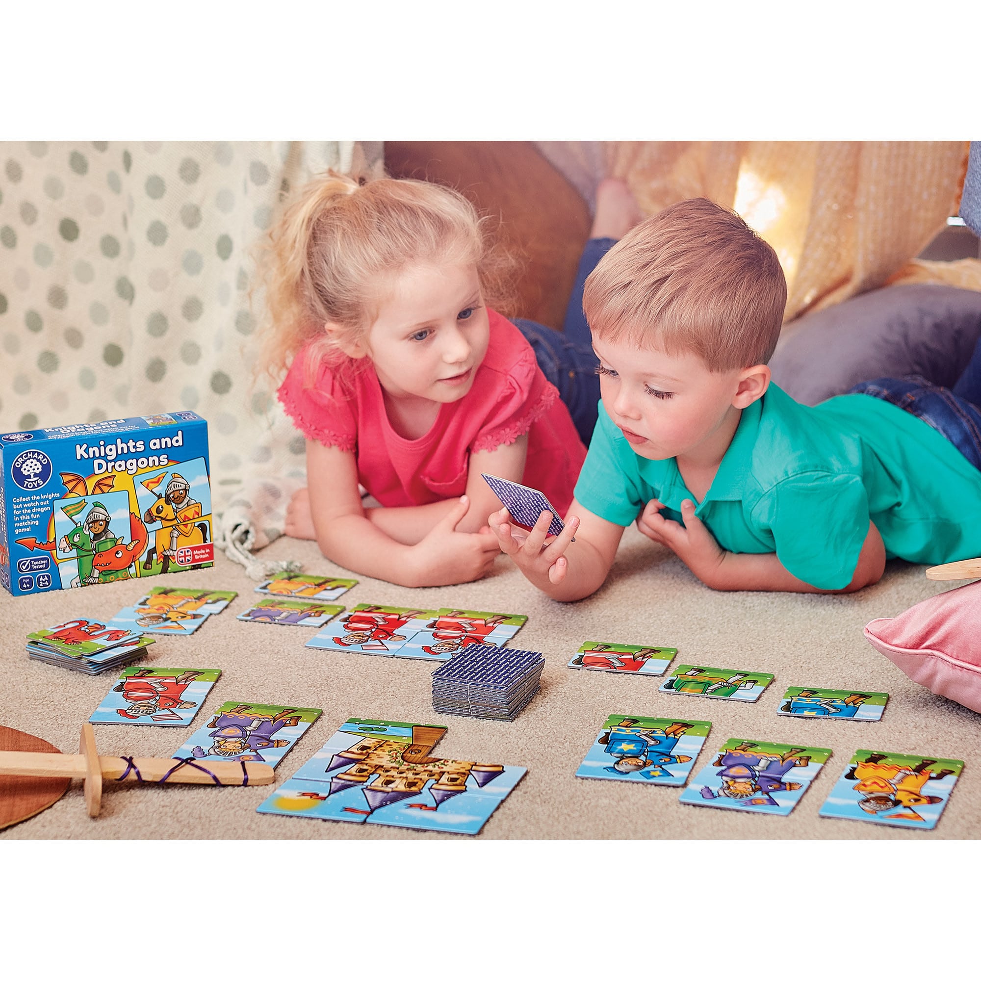 Two children playing with a 'Knights and Dragons' card game on the floor.